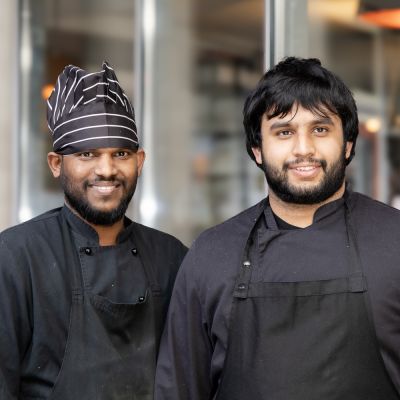 Zwei Küchenmitarbeiter in schwarzer Uniform, einer davon mit gestreifter Kochmütze.