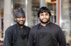 Zwei Küchenmitarbeiter in schwarzer Uniform, einer davon mit gestreifter Kochmütze.