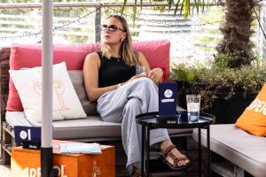 Eine Frau mit Sonnenbrille sitzt auf gepolsterten Palettenmöbeln auf einer Dachterrasse.