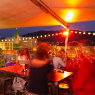 Gut besuchte Dachterasse am Abend, mit Blick auf die Stadtkulisse.