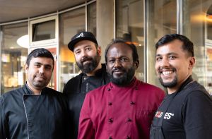 Eine Gruppe von vier Männern in unterschiedlicher schwarzer und weinroter Gastronomie-Arbeitskleidung.